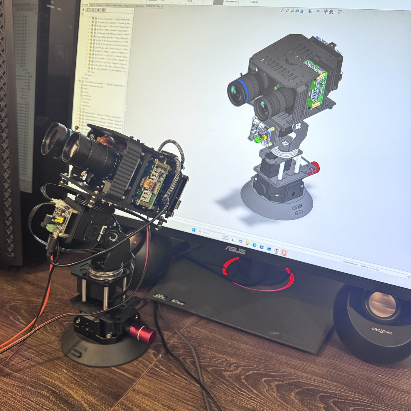 The GW-VSR1 visual module on a desk: two cameras with black lenses on a motorised pan-tilt head above a suction-cup mount, with its CAD model on the monitor behind it.